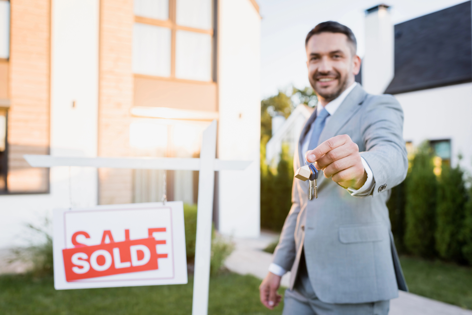Smiling broker holding keys near sold sign Smiling broker holding keys near sold sign